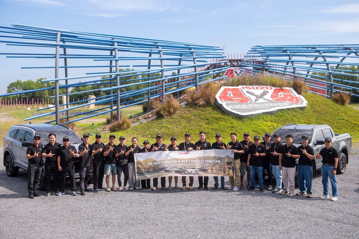 Đoàn khách hàng chụp ảnh cùng banner hội thảo bên đường thử, phía sau có xe Isuzu