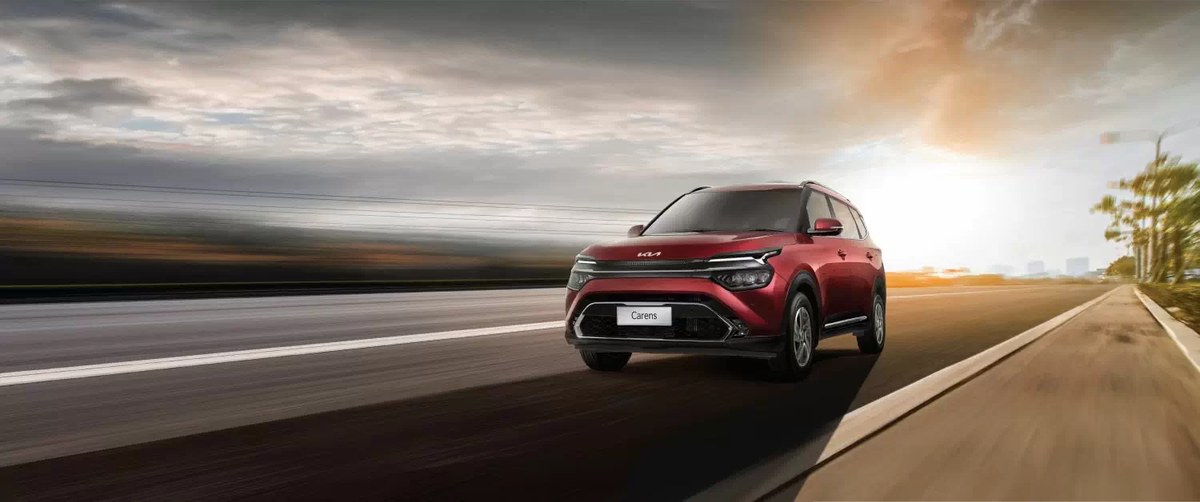 Kia Carens màu đỏ chạy trên đường vắng