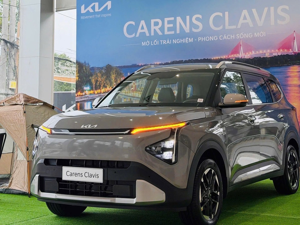 Kia Carens Clavis màu xám trưng bày trước phông nền cầu dây văng tại showroom Kia Cần Thơ