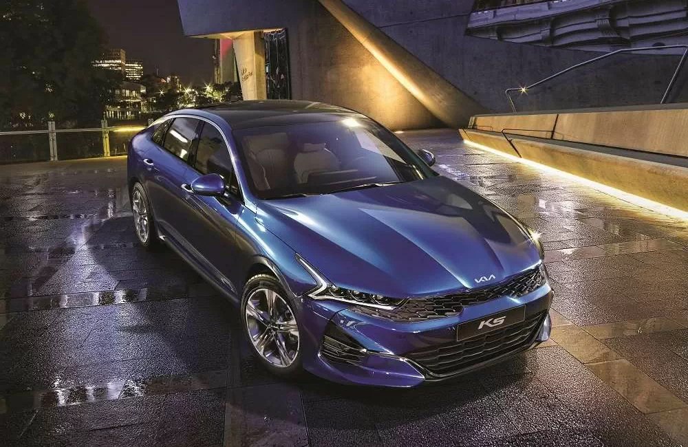 Kia K5 màu xanh trên mặt đường ướt lúc tối
